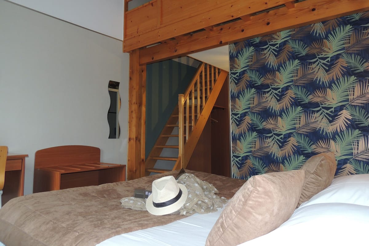 Un dormitorio con una cama litera, una escalera de madera, un papel pintado decorativo y una cama con un sombrero y una almohada.