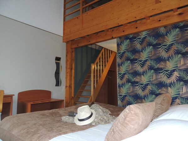 A bedroom with a bunk bed, a wooden staircase, a patterned wall, and a bed with a hat and pillow. - Hotel Les Trois Marchands (Bressuire)
