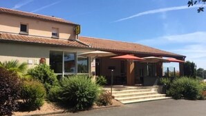 Un bâtiment doté d’un toit recouvert de tuiles, d’une entrée abritée avec des marches et d’un espace de stationnement.