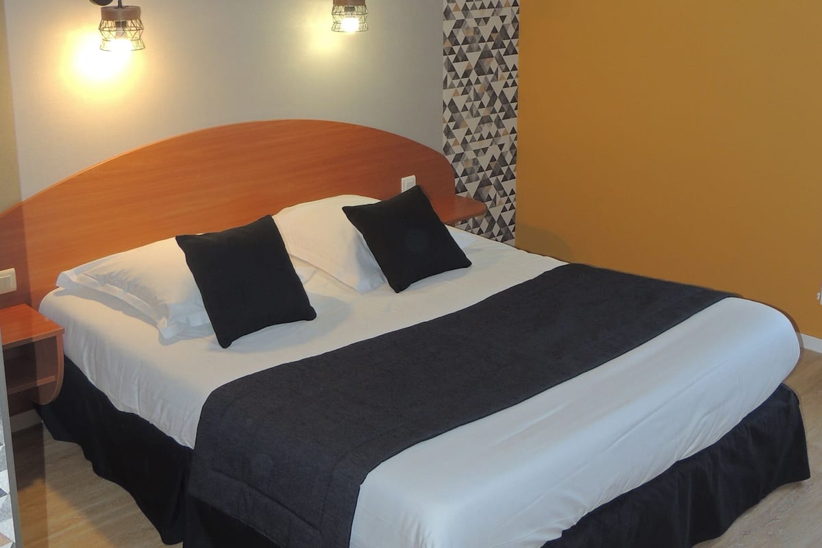 Una cama bien hecha con cabecera de madera, dos mesitas de noche y un papel tapiz estampado.