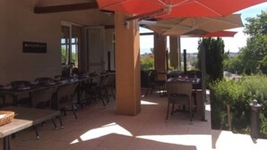 Un espace extérieur aménagé en terrasse, avec des tables et des chaises, un parasol rouge et une enseigne indiquant « RESTAURANT ».