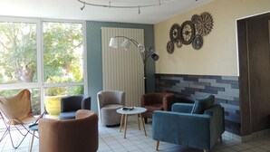 Un espace lounge moderne offrant de nombreuses options d’assise, un mur décoratif orné d’engrenages et une grande fenêtre donnant sur un paysage verdoyant.