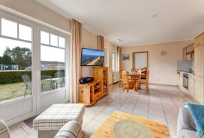 Ein großzügiger Wohnbereich mit einem großen Fernseher, Holzmöbeln und Blick ins Freie.