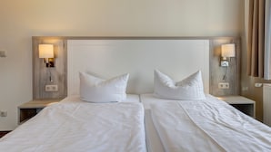 Habitación de hotel con dos camas, cada una con ropa blanca y almohadas, y lámparas de pared a cada lado.