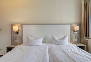 A hotel room with two beds, each with white bedding and pillows, and wall-mounted lamps on either side.