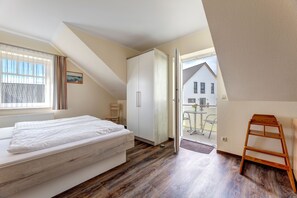 A bedroom with a bed, a wardrobe, a wooden ladder, and a view of the outside.