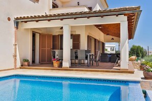 A covered outdoor area with a pool, seating, and a view of the surrounding landscape.