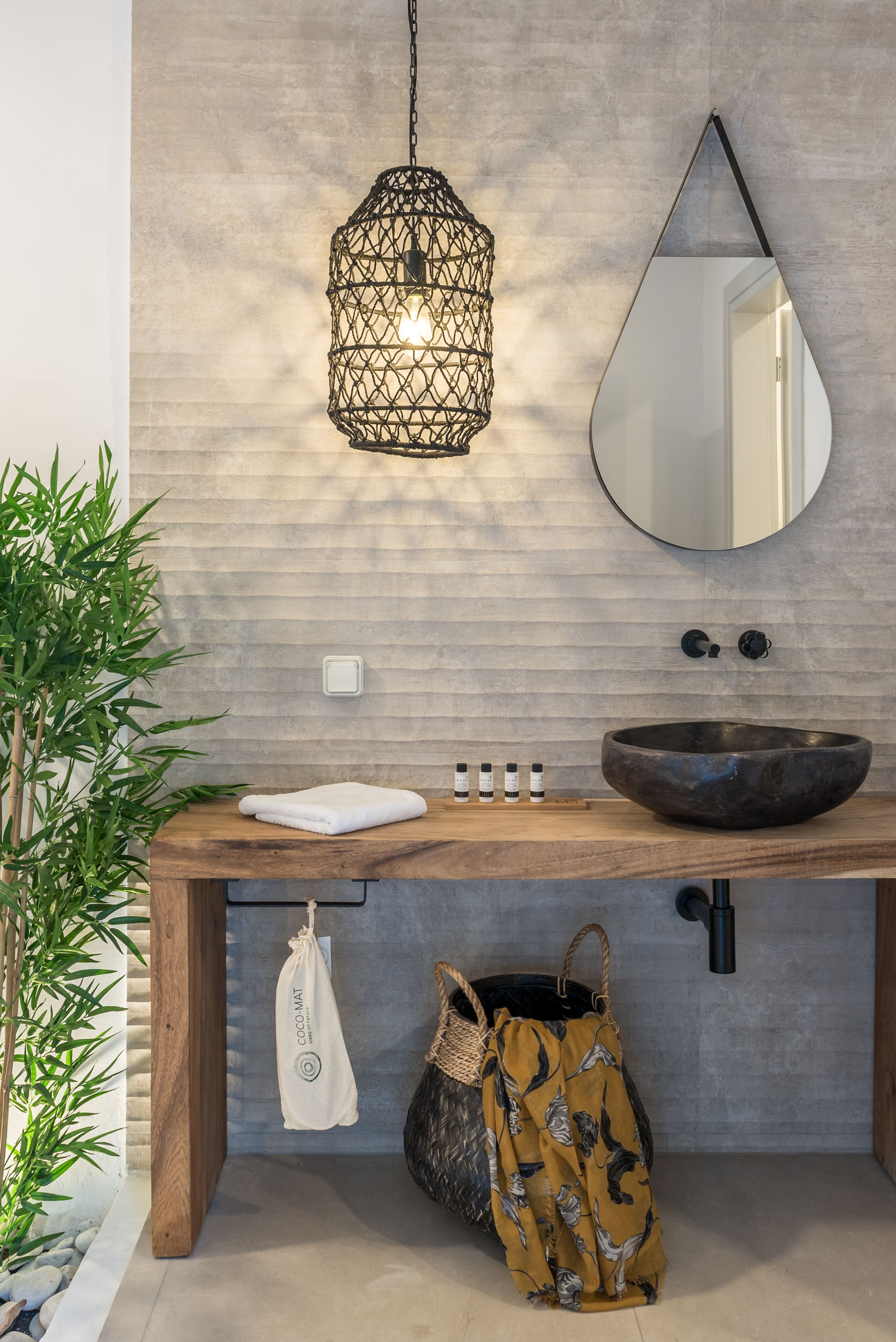 Une salle de bain avec un meuble-lavabo en bois, un miroir rond, un luminaire suspendu et une plante en pot.