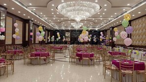 Un amplio salón de banquetes con mesas redondas, sillas doradas y una gran lámpara de araña.