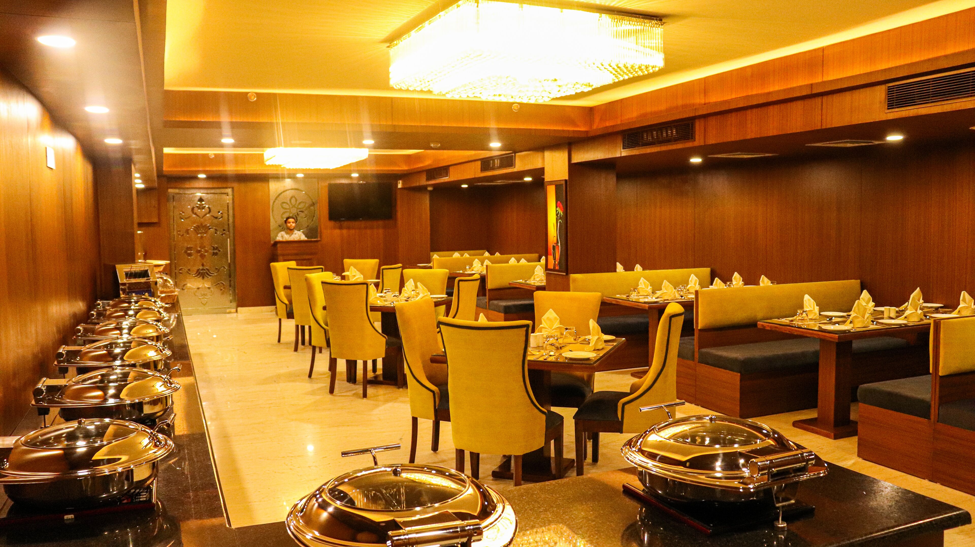 Restaurante com várias mesas e cadeiras, um buffet com pratos cobertos e um candelabro.