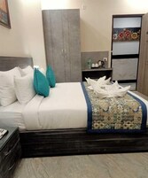 A hotel room with a bed, a wardrobe, a nightstand, and a painting on the wall.