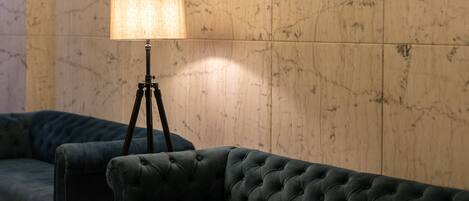 A dark green tufted sofa and a floor lamp with a beige lampshade in a room with wooden panel walls.