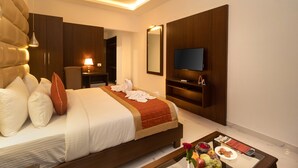 Una habitación de hotel moderna con una cama grande, televisión, escritorio con lámpara y una mesa de centro con alimentos para el desayuno.