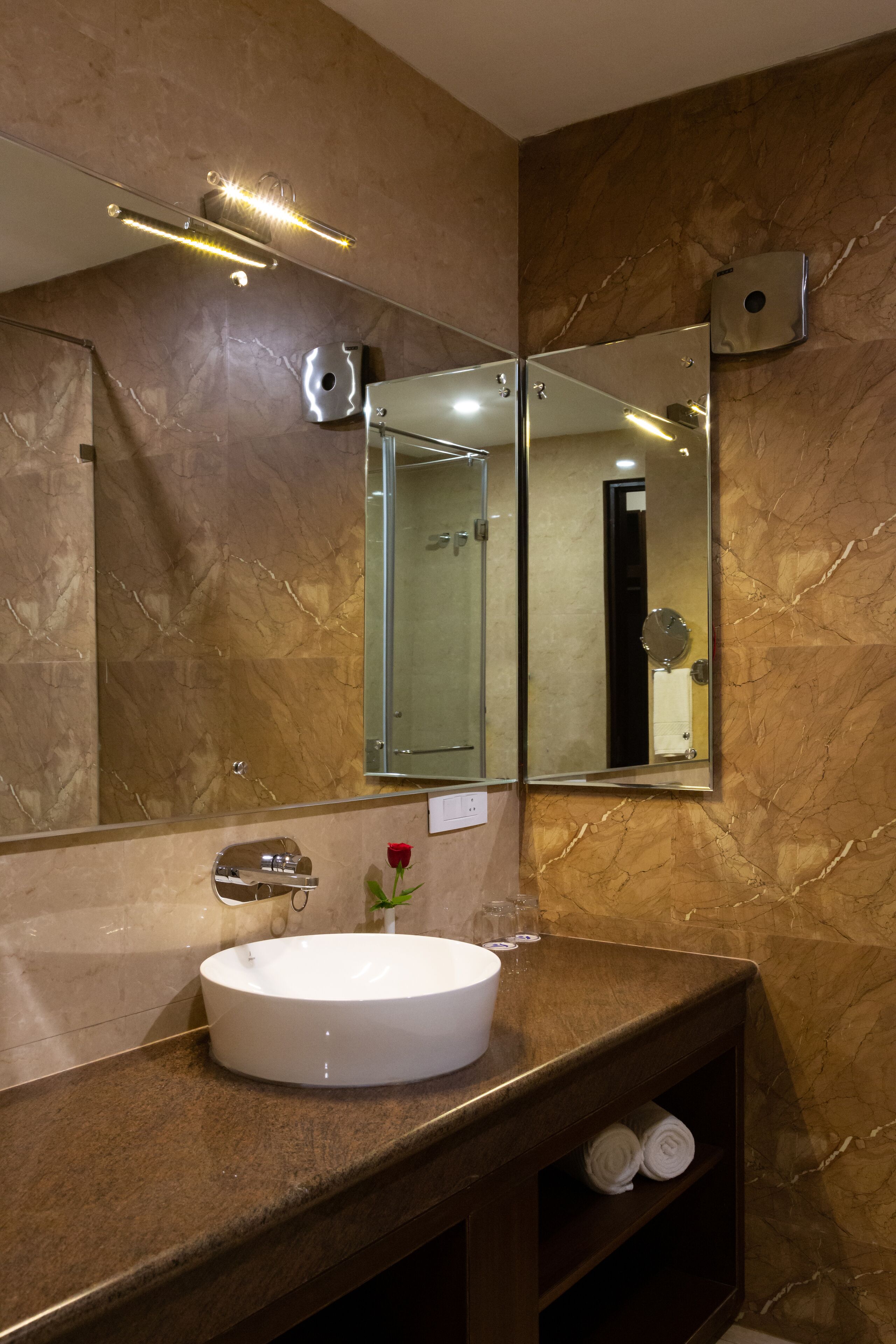 Un baño con pared de mármol, un lavabo blanco redondo, un espejo y un perchero para toallas.