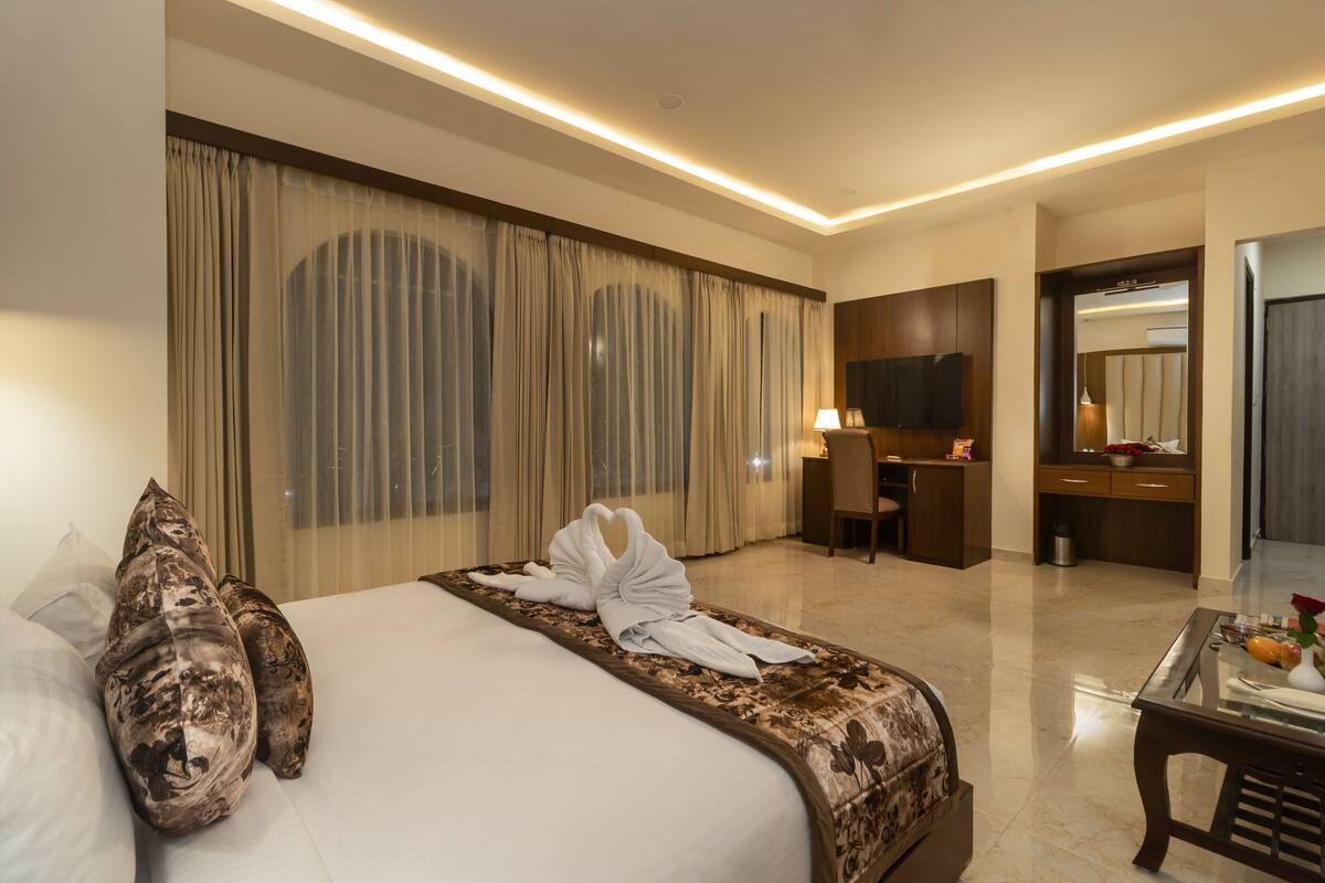 Habitación de hotel con una cama grande, un escritorio, televisión y un baño visible a través de una puerta abierta.