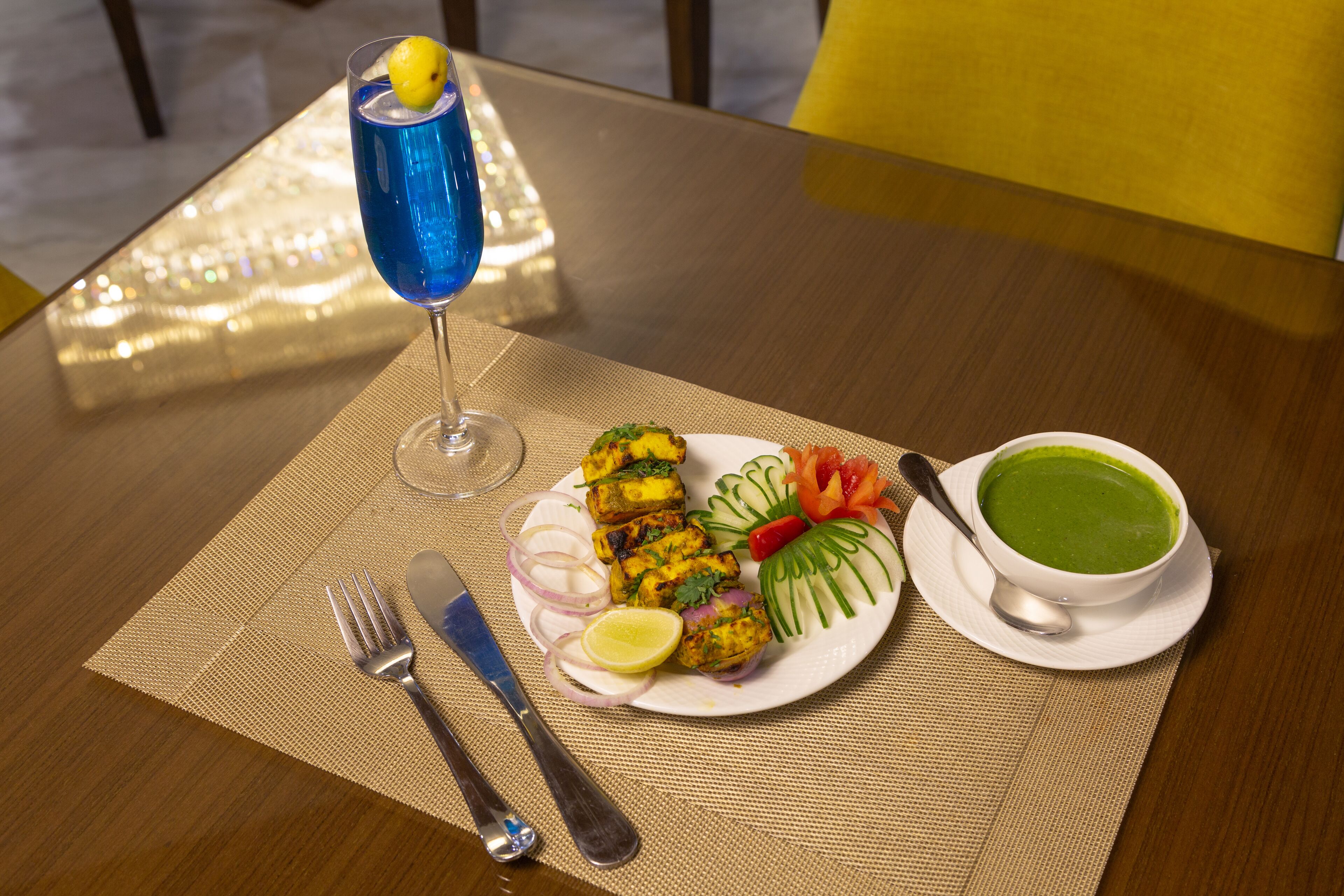 Een gedekte tafel met een bord eten, een soepkom en een glas blauwe drank.