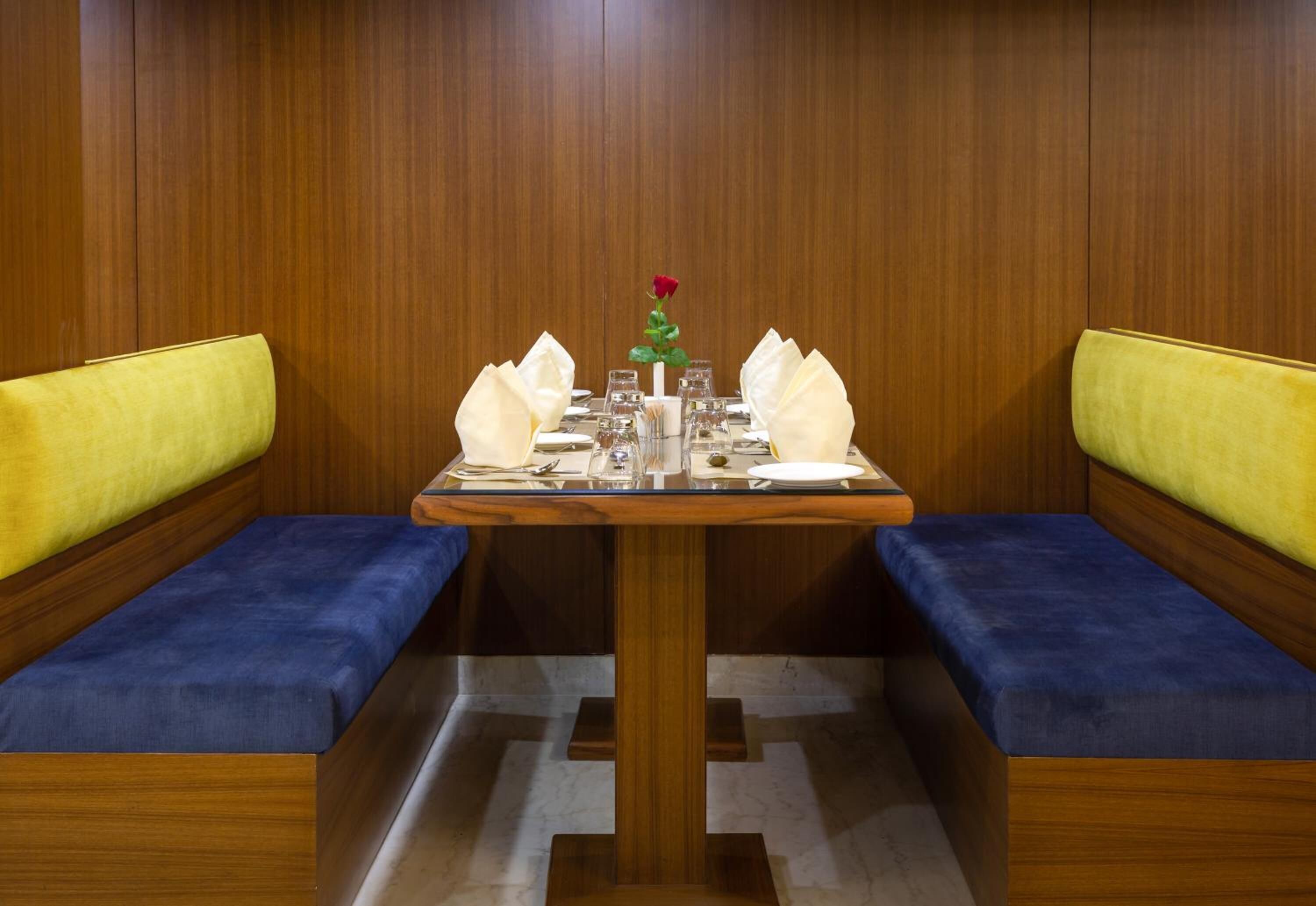 A dining area with a wooden booth table, white napkins, and a single red rose centerpiece.
