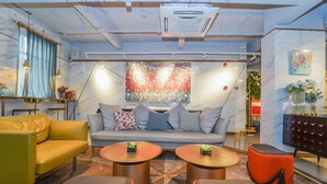 A modern lounge area with a sofa, yellow and grey armchairs, and round tables with potted plants. - No. 8 Art Hotel (Shanghai)
