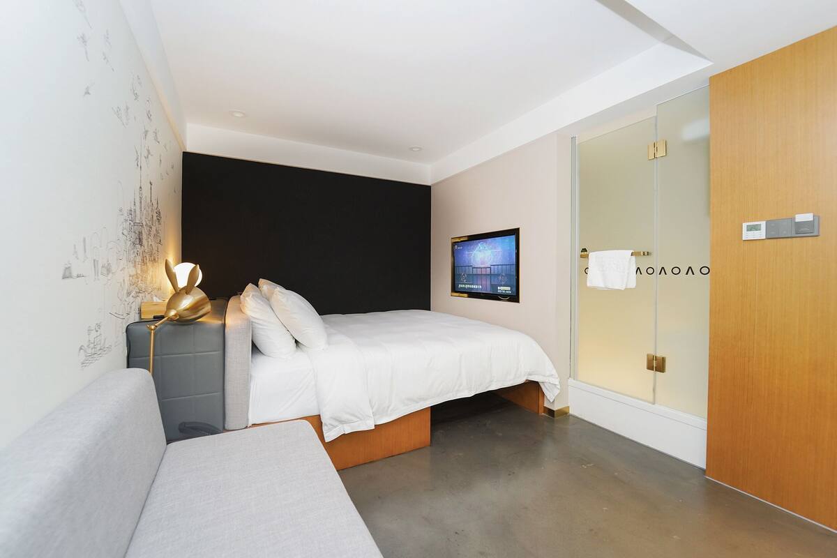 A modern bedroom with a bed, a bedside table, a wall-mounted TV, and a wooden wardrobe.