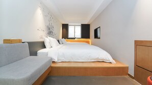 A modern bedroom with a bed, a sofa, a wooden platform, a TV, and a wall with a cityscape mural. - No. 8 Art Hotel (Shanghai)