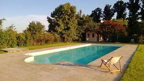 Une piscine rectangulaire dotée d’une terrasse dallée, entourée d’une pelouse bien entretenue et d’arbres.
