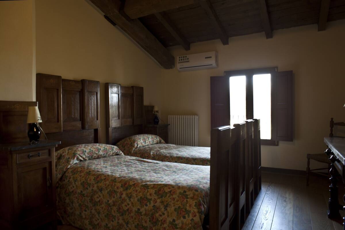 Une chambre à coucher avec deux lits en bois, une table de chevet, une lampe, une commode et une fenêtre avec des volets.