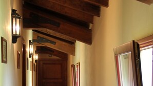 Un couloir étroit avec des poutres en bois, un banc et une fenêtre dotée d’un cadre rouge.