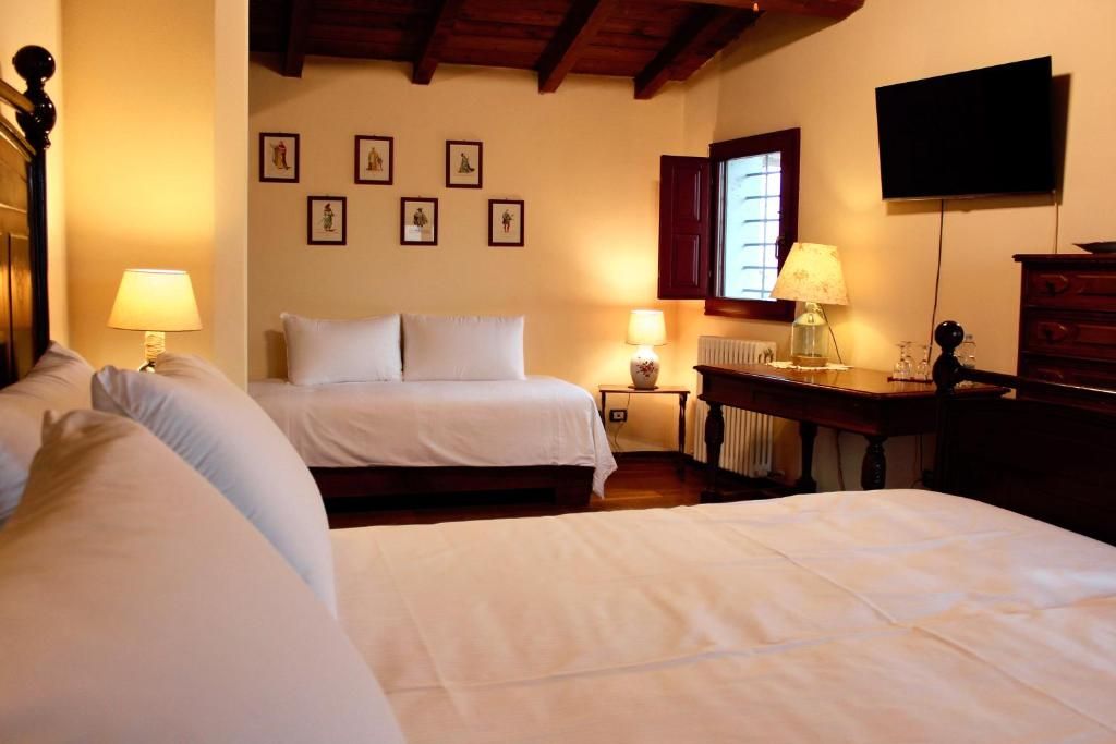 A hotel room with two beds, a desk, a chair, a television, and framed pictures on the wall.