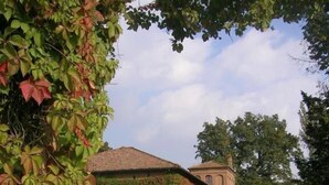 Un bâtiment à la façade en briques, partiellement recouverte de lierre, avec une allée gravillonnée et un ciel dégagé.
