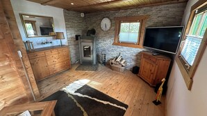 Interior acogedor de una cabaña con pared de piedra, techo de madera, chimenea, televisor y un mueble de madera.