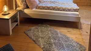 Un dormitorio acogedor en el ático, con techo inclinado, cama con ropa de cama estampada, mesita de noche con lámpara y ventana con cortinas.