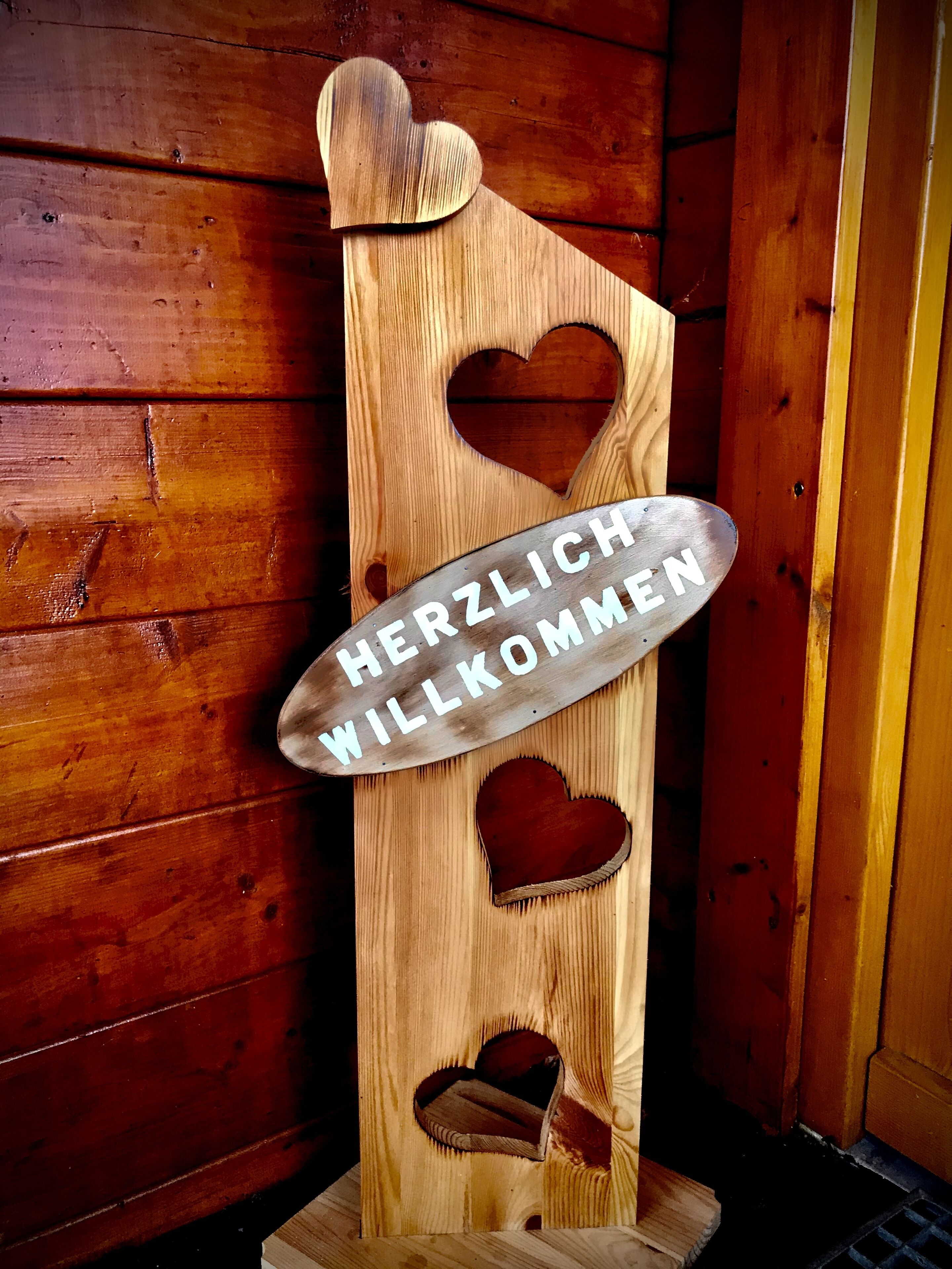 A wooden sign with heart-shaped cutouts and the text "HERZLICH WELCOME".