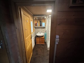 A wooden hallway leading to a bathroom with a sink, mirror, and towel rack.