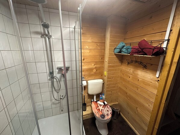 Un baño pequeño con ducha, inodoro y paredes de madera.