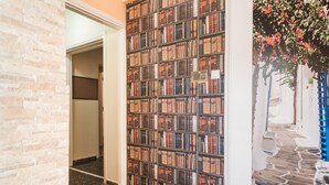 A hallway with a bookshelf wall, a stone floor, and a doorway leading to another room. - Athens Cozy Rooms (Athens)