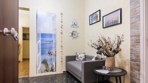 A room with a sofa, a small table, a decorative vase, a wall clock, and a door leading to another room. - Athens Cozy Rooms (Athens)