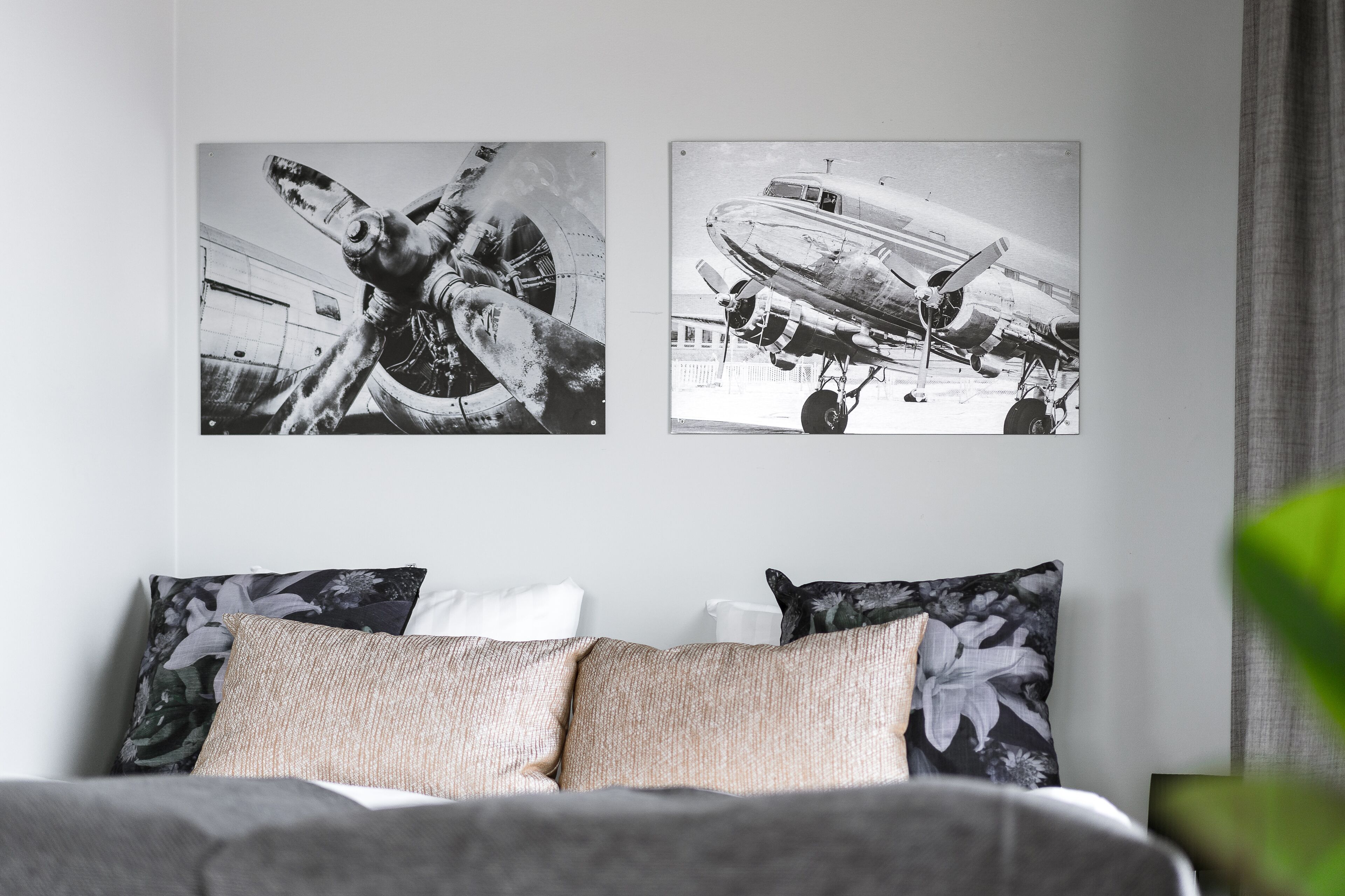 Un dormitorio con una cama, dos almohadas y dos fotografías en blanco y negro de aviones.