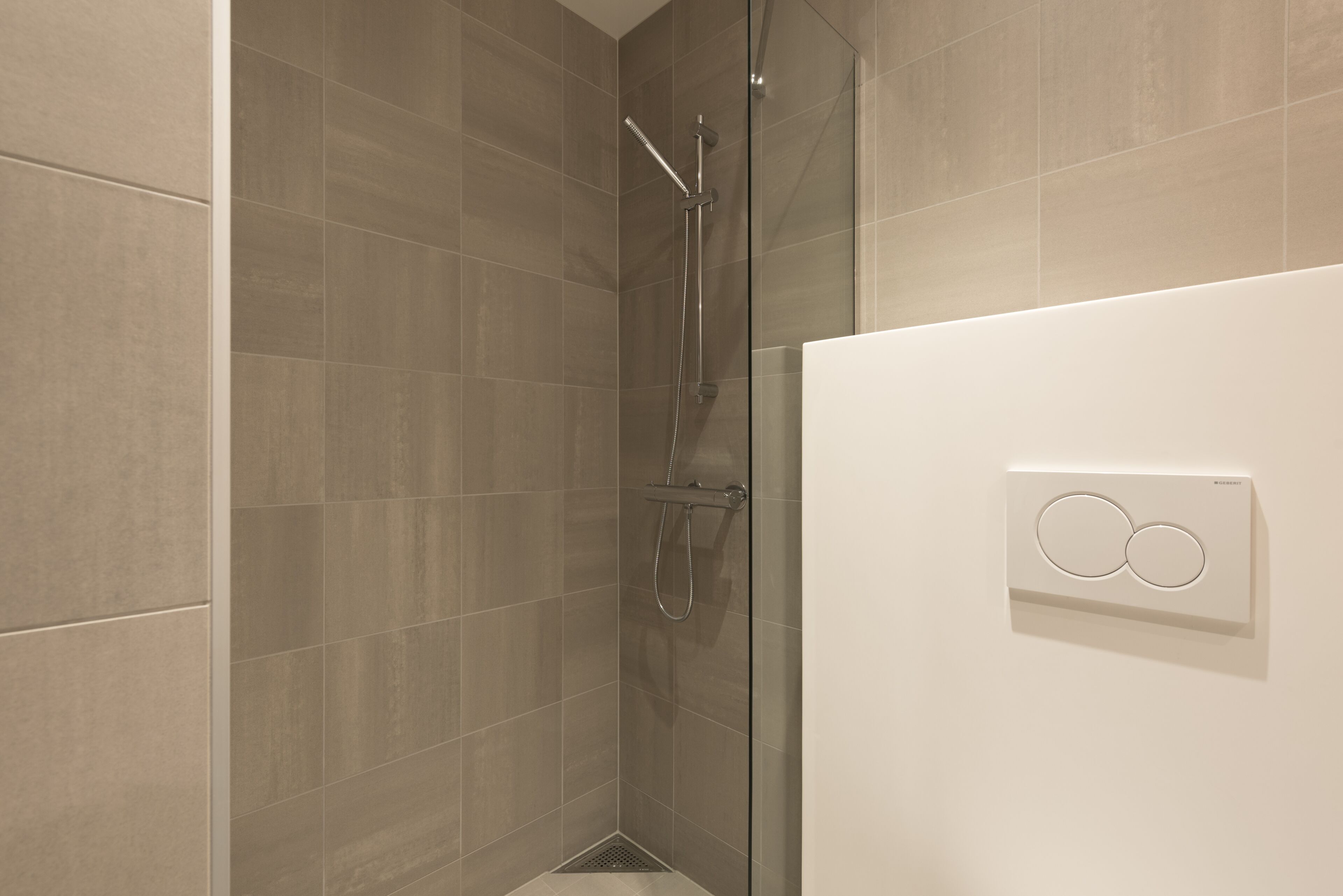 A modern bathroom with a glass-enclosed shower, a white wall-mounted control panel, and a tiled floor.