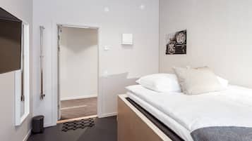 Una habitación de hotel moderna con una cama, un cesto de basura pequeño, una puerta y una lámpara fijada a la pared.
