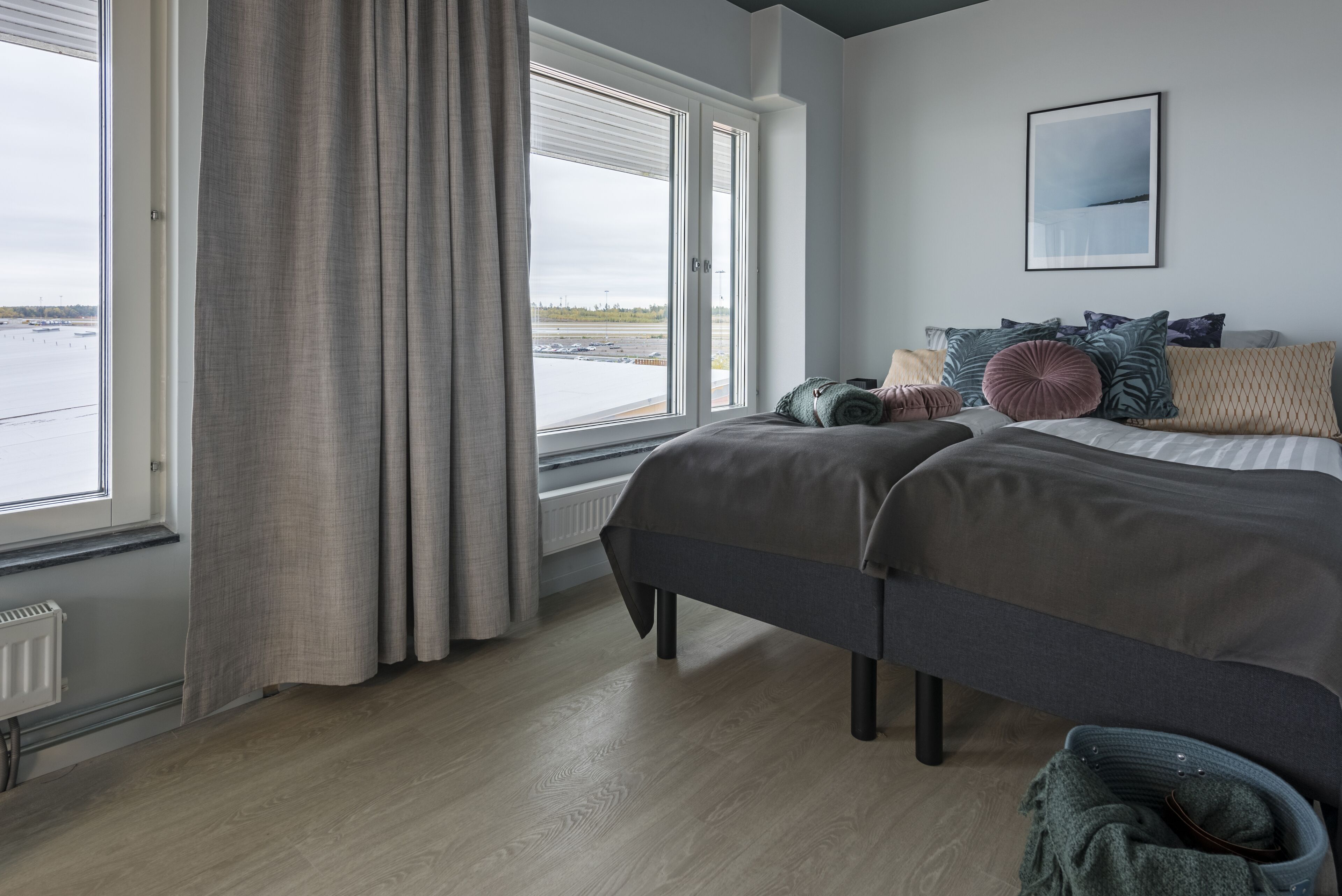 A bedroom with a large window, a bed with multiple pillows, and a radiator.