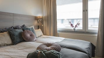 A neatly made bed with multiple pillows and a blanket, a bedside lamp, and a window with a view of a building.