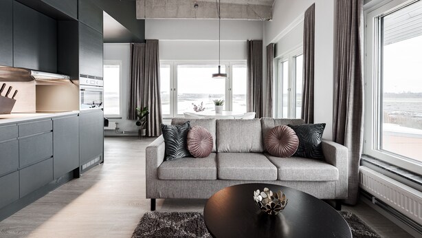 A modern living room with a grey sofa, black coffee table, and large windows offering a view of the city. - Forenom Aparthotel Arlanda (Arlanda)