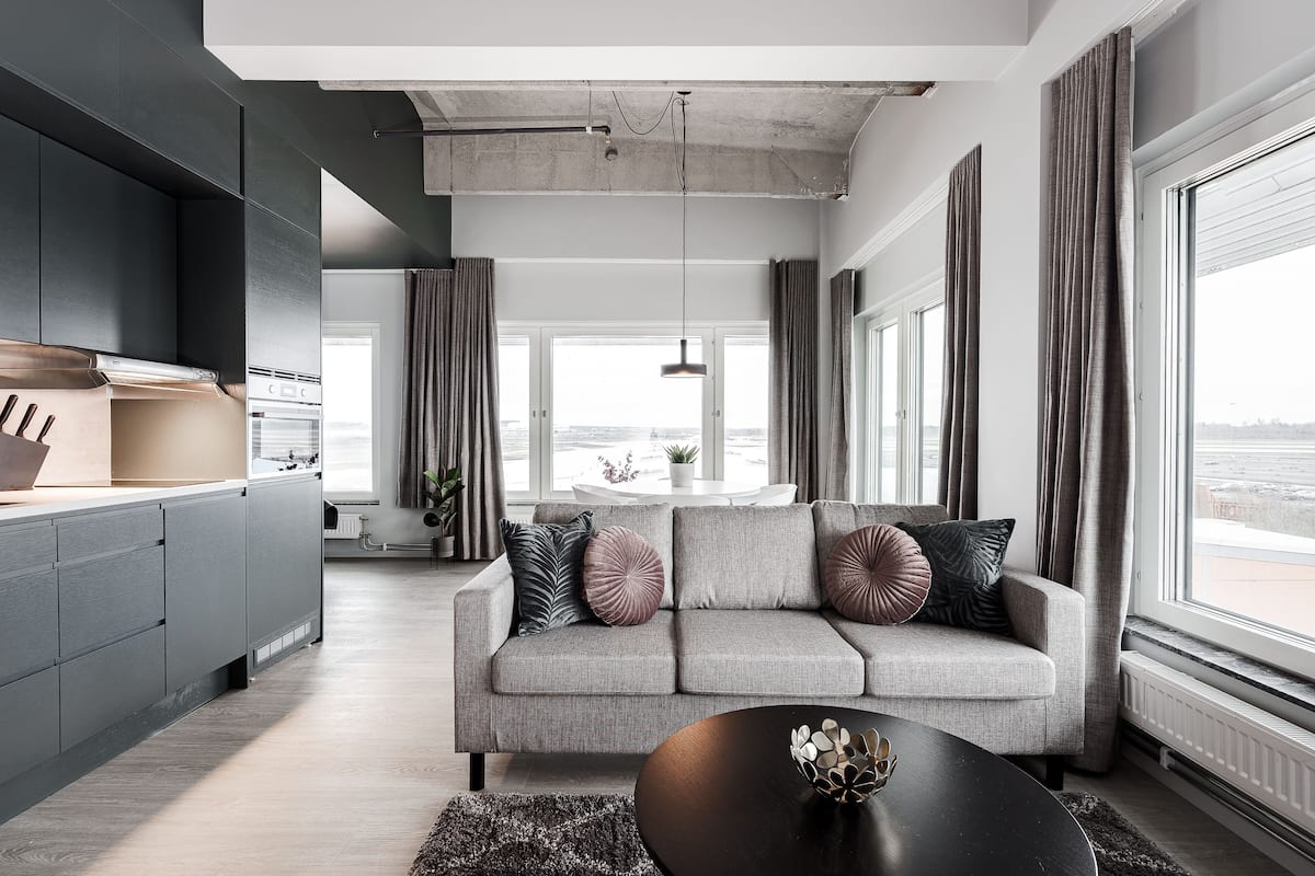 Ein modernes Wohnzimmer mit grauem Sofa, einem schwarzen Couchtisch und großen Fenstern mit Blick auf die Stadt.
