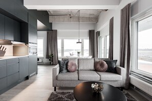 A modern living room with a grey sofa, black coffee table, and large windows offering a view of the city. - Forenom Aparthotel Arlanda (Arlanda)