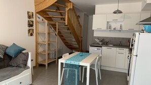 A compact apartment with a kitchenette, a dining area, and a staircase leading to an upper level. - Charming Cottage Near Quend Beach: 2BR, Garden, Parking (Quend)