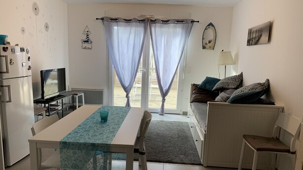 A modern kitchen with a refrigerator, a dining table with a patterned tablecloth, and a television. - Charming Cottage Near Quend Beach: 2BR, Garden, Parking (Quend)