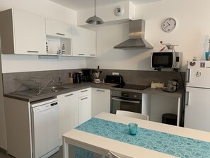 Una cocina moderna con armarios blancos, una campana extractora de acero inoxidable, un microondas, un refrigerador y una mesa de comedor con mantel azul.