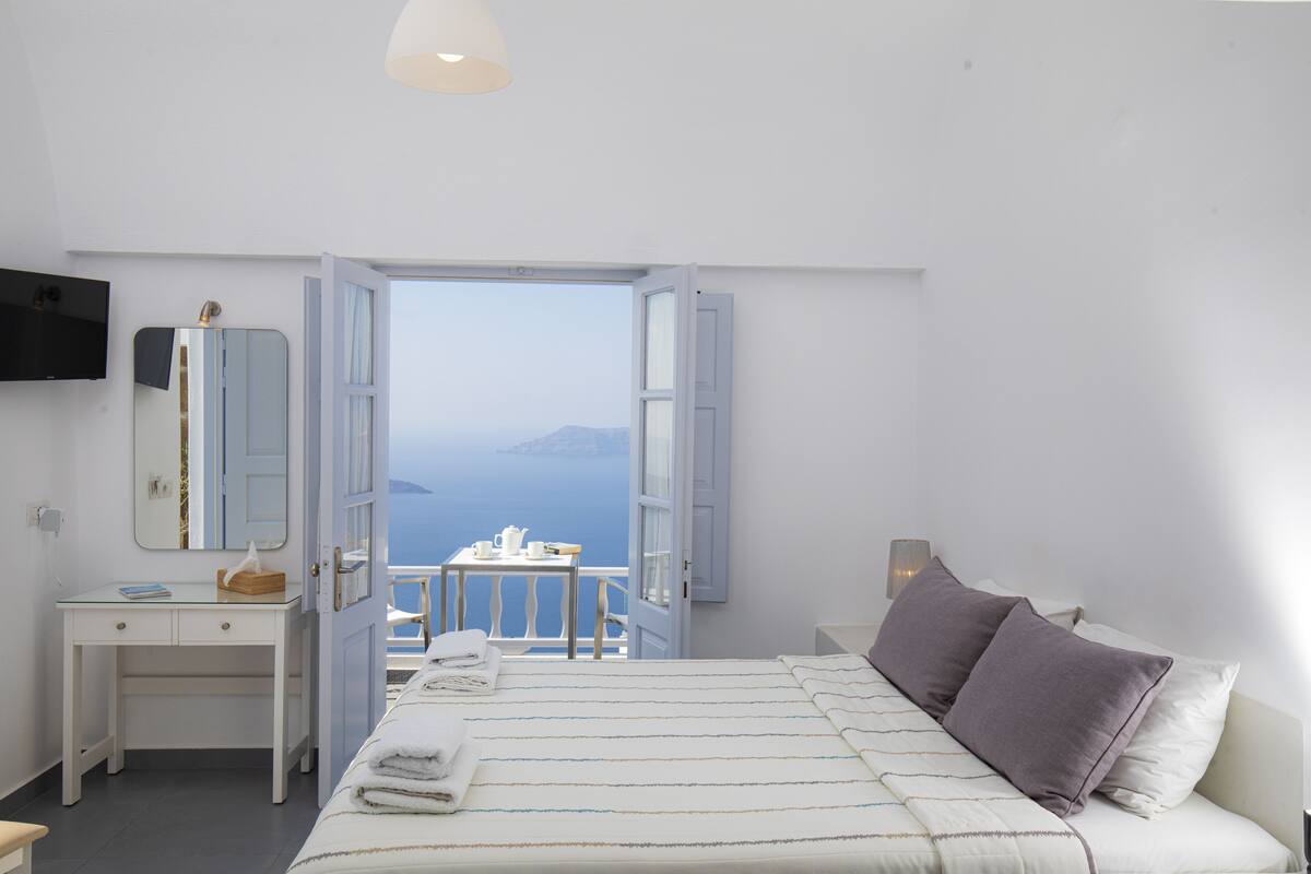A bedroom with a bed, a desk, a chair, and a view of the sea.