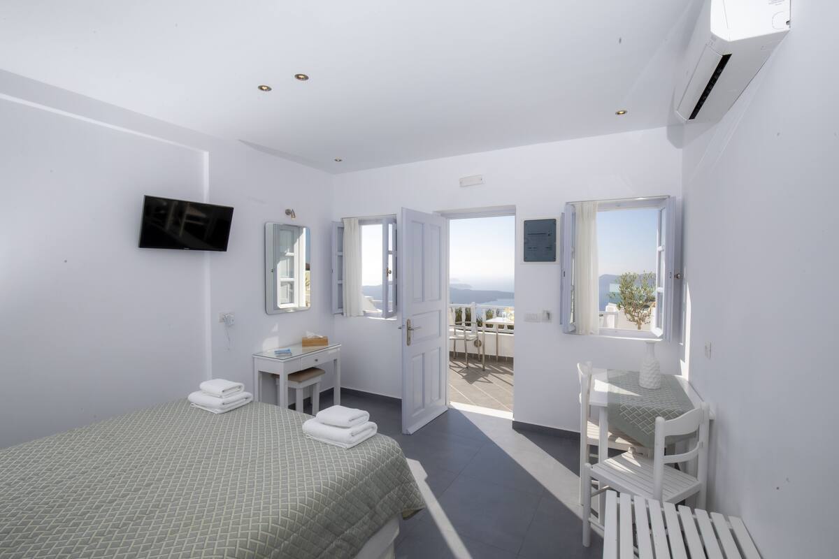 A hotel room with a bed, a desk, a chair, a TV, and a balcony with a view.