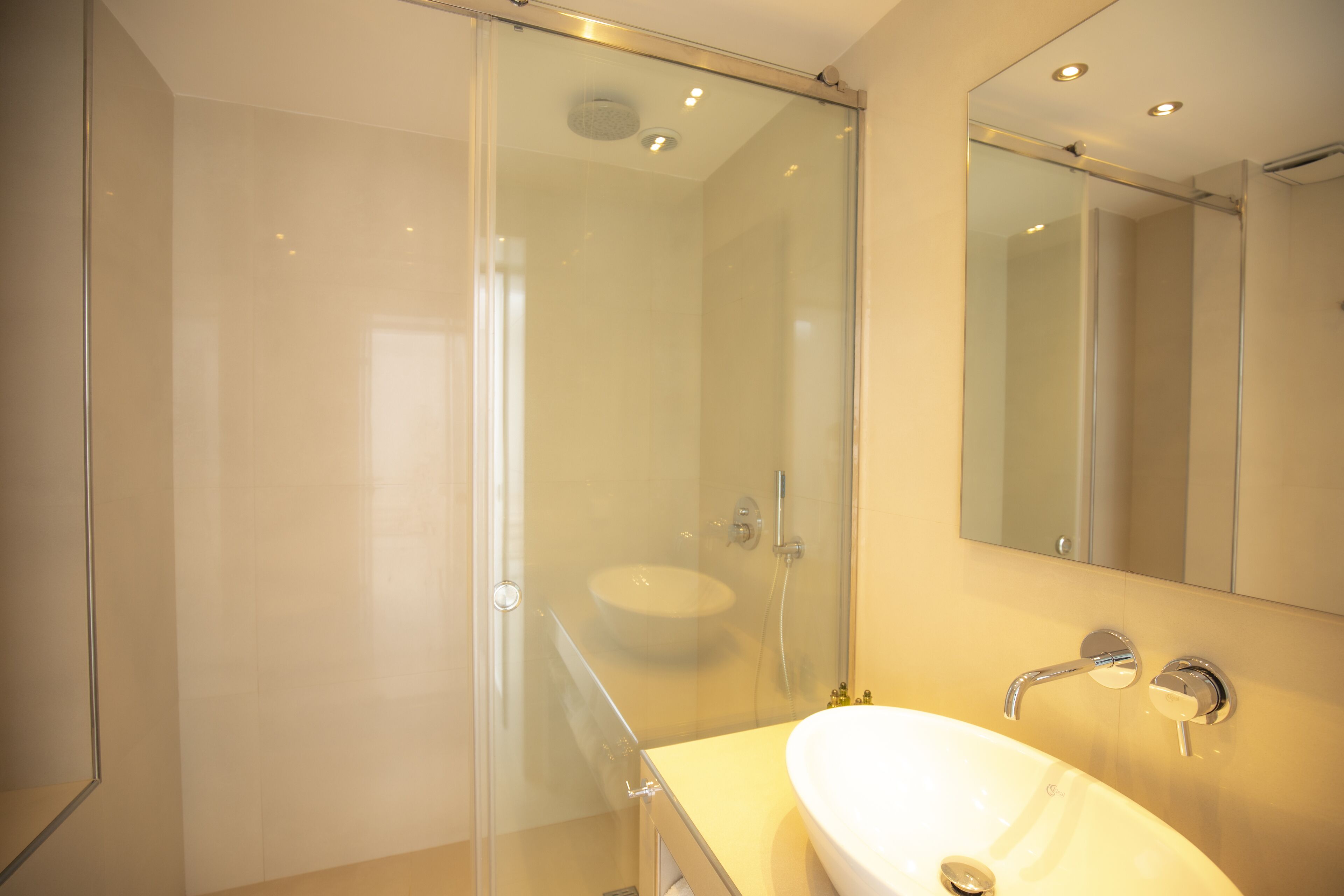 Un baño moderno con cabina de ducha de vidrio, un lavamanos blanco y un espejo grande.